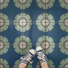 a person's feet standing on a tiled floor with blue and green tiles in the background