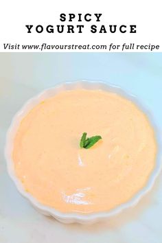 a white bowl filled with yellow sauce on top of a blue tablecloth next to a green leaf