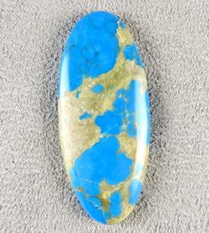 a blue and yellow stone laying on top of a gray carpet next to a white wall