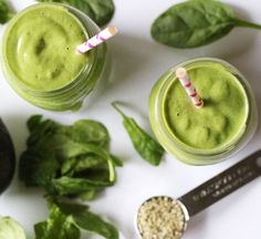 two glasses filled with green smoothie next to an avocado and straws