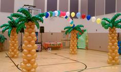 some palm trees and balloons are on the floor in an indoor basketball court for a birthday party