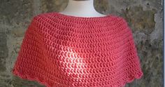 a pink crocheted ponchle on a mannequin head stand in front of a stone wall