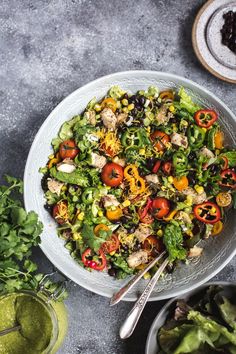 a salad with chicken, tomatoes and black olives in a white bowl on a gray table