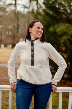 a woman standing next to a white fence with her hands on her hips and smiling