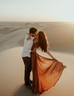 a man and woman kissing in the desert with sand dunes in the back ground behind them