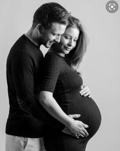 a pregnant couple cuddles while posing for a black and white photo in the studio