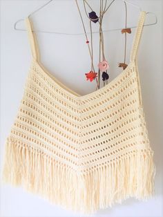 a crocheted crop top hanging on a clothes hanger with flowers in the background