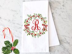 the monogrammed dish towel is next to a candy cane and holly wreath on a marble countertop