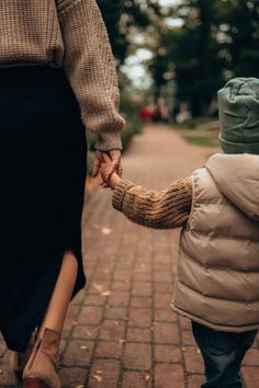 a woman holding the hand of a small child who is walking down a brick path