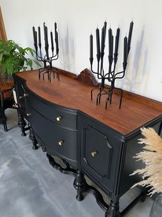 an old dresser has many black candles on it and is next to a potted plant