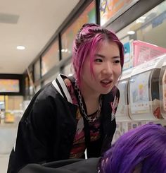 a woman with pink hair is looking at something in a refrigerator while another person looks on