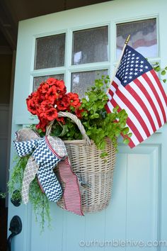 a basket filled with flowers sitting on top of a blue door next to an american flag