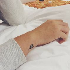 a person's hand with a small tattoo on their left wrist, resting on a bed