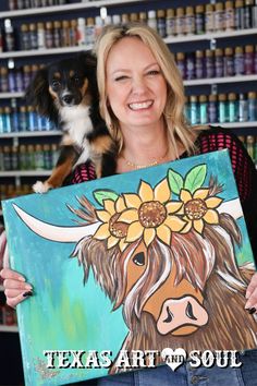 a woman holding up a painting with a dog on her lap next to the sign that says texas art and soul