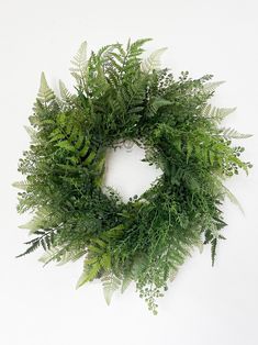 a green wreath on a white wall with lots of greenery in the center and leaves around it