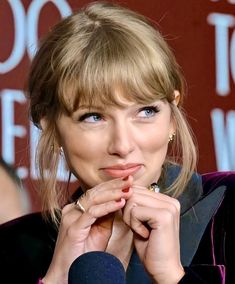 a woman with blue eyes and blonde hair is holding her hand to her mouth while wearing a purple velvet jacket