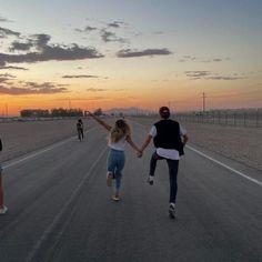 two people holding hands while walking down an empty road at sunset in the middle of nowhere