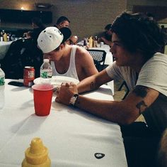 two young men sitting at a table eating food and drinking soda in front of them