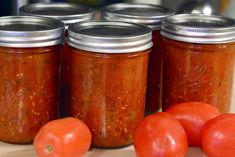 tomatoes and other vegetables sit in jars on a table