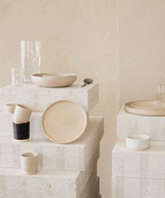 three stacks of white plates and bowls on top of each other in front of a beige wall