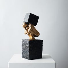 a sculpture of a man with a block on his head sitting on top of a block