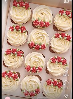 twelve cupcakes with white frosting and red flowers in a box on a table