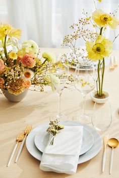 the table is set with white plates, silverware and yellow flowers in vases