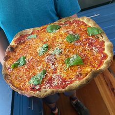 a person holding up a pizza with cheese and basil on it's crusts