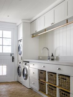 a washer and dryer in a white laundry room with wood flooring, built - in cabinets and drawers