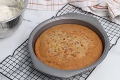 a cake in a pan on a cooling rack next to a bowl of whipped cream