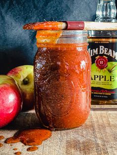 an apple cider and two apples on a table with jam in the jar next to it