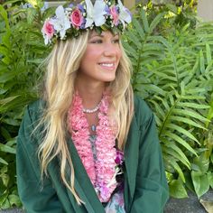 a woman with flowers in her hair wearing a green jacket and pink flower lei around her neck