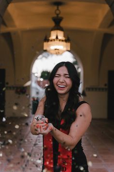 a woman is smiling and throwing confetti in the air while standing on a tiled floor