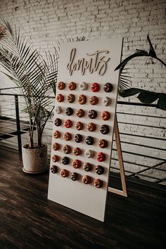 a sign with donuts on it sitting next to a potted plant and brick wall