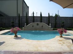 a small pool in the middle of a backyard with flowers on each side and an umbrella over it