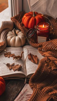 an open book sitting on top of a window sill next to some pumpkins