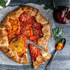 a pizza with tomatoes and herbs on the top is cut into four pieces, sitting on a piece of parchment paper