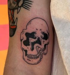 a black and white skull tattoo on the left arm with an eagle flying above it