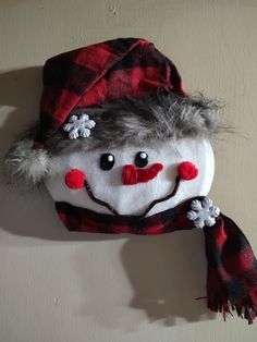 a stuffed snowman wearing a red and black plaid hat with pom poms