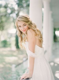 a woman in a white dress leaning on a wall