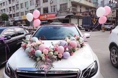 a car decorated with balloons and flowers on the hood is parked in front of other cars