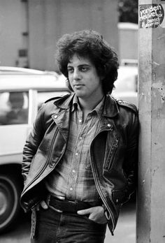 a black and white photo of a man leaning against a pole