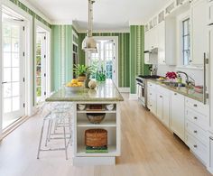 a kitchen with white cabinets and green wallpaper, an island in the center is surrounded by stools