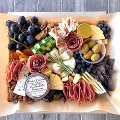 an assortment of cheeses, meats and vegetables arranged in a square tray on a wooden table