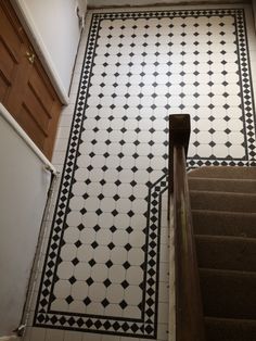 a staircase with black and white tiles on the floor, next to a brown door