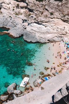 people are swimming in the clear blue water next to rocky cliffs and beach umbrellas