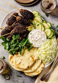 a plate filled with meat skewers, cucumbers and other food items