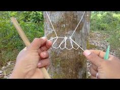 two hands are working on a piece of string art in front of a tree trunk