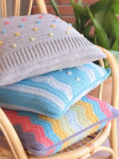 four crocheted pillows stacked on top of each other in front of a potted plant