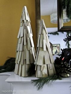 two wooden christmas trees sitting on top of a mantle next to a mirror and pine cones